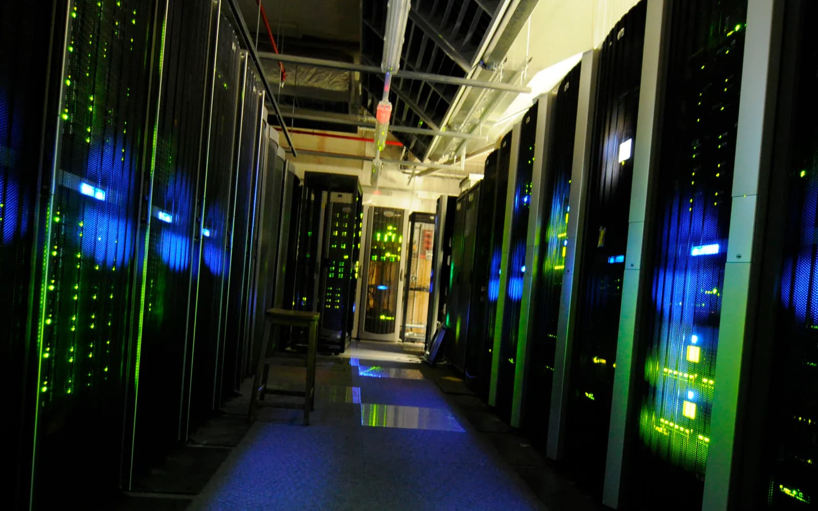 Dark server-room aisle lined with black cabinets and blue-green equipment lights.