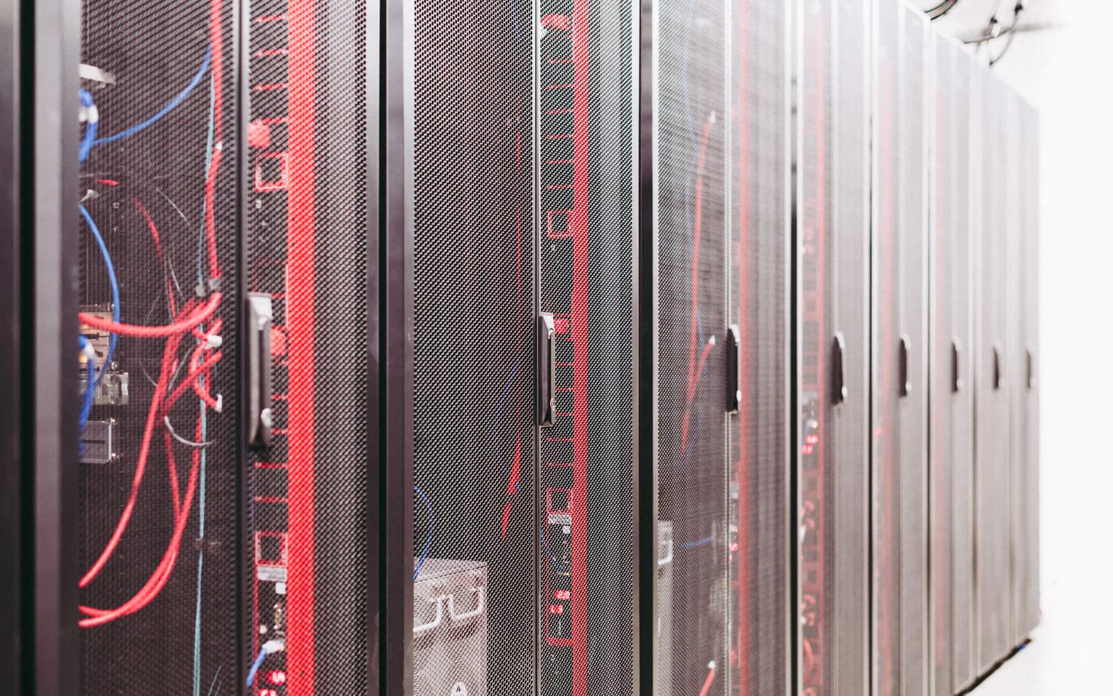 Rows of black server cabinets with red cables leading toward a bright data-center aisle.