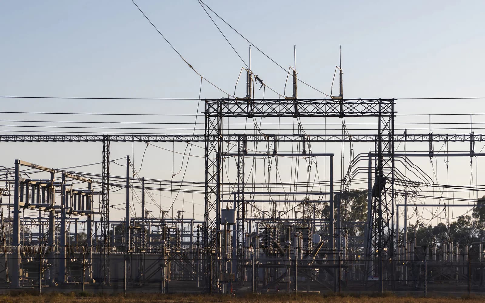 Electrical substation steelwork, insulators, and lines at dawn.