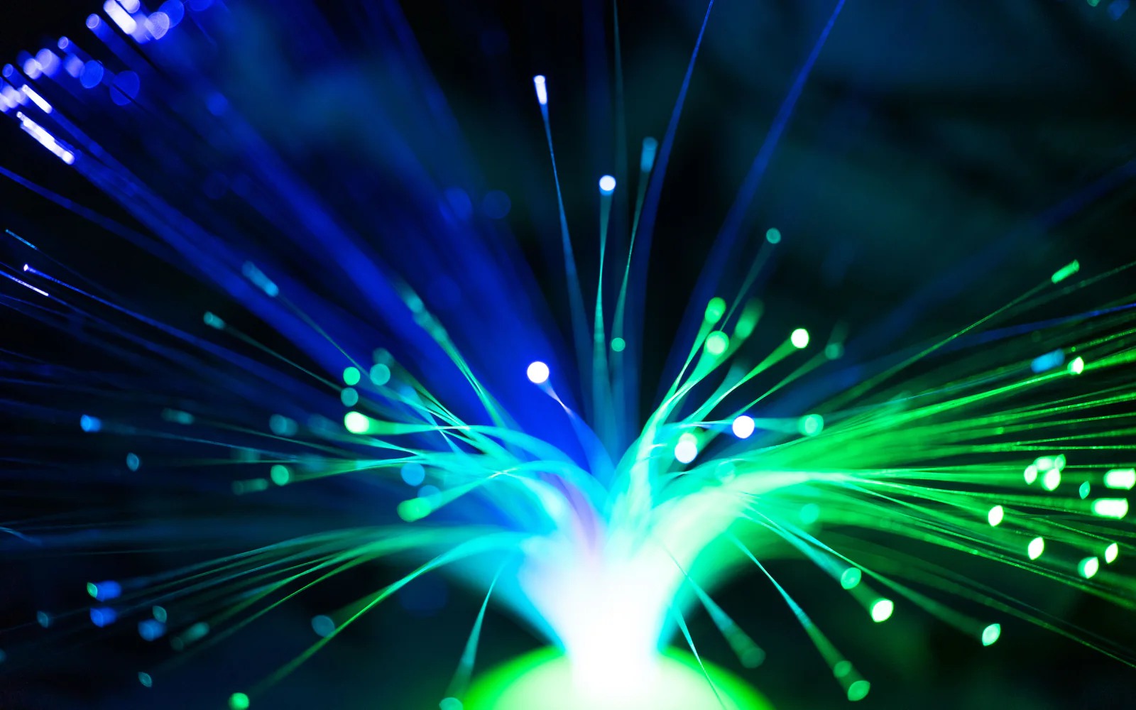 Blue and green optical fibers radiate from a bright point against black.