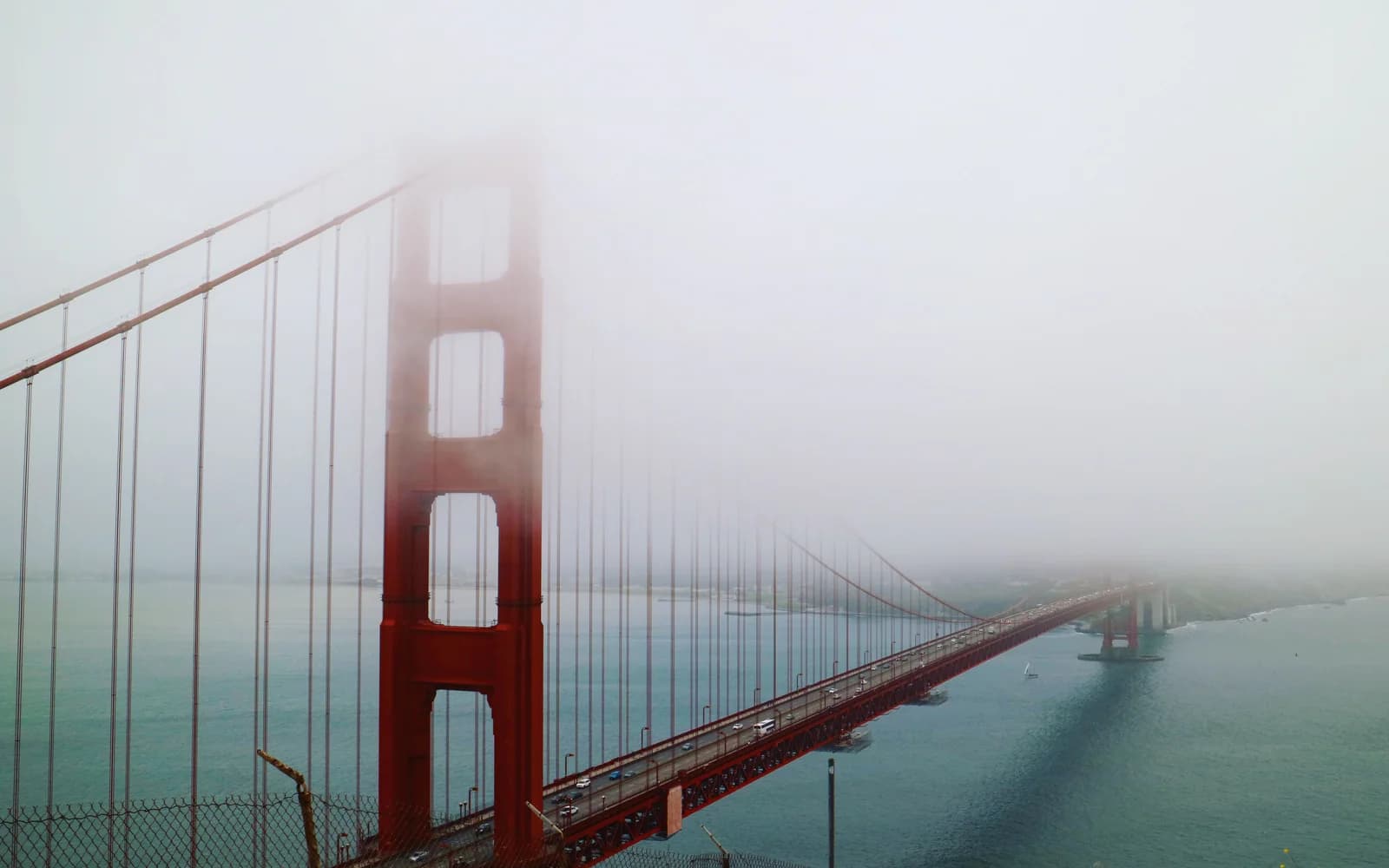 Golden Gate Bridge stretching over blue-gray water and disappearing into dense fog.