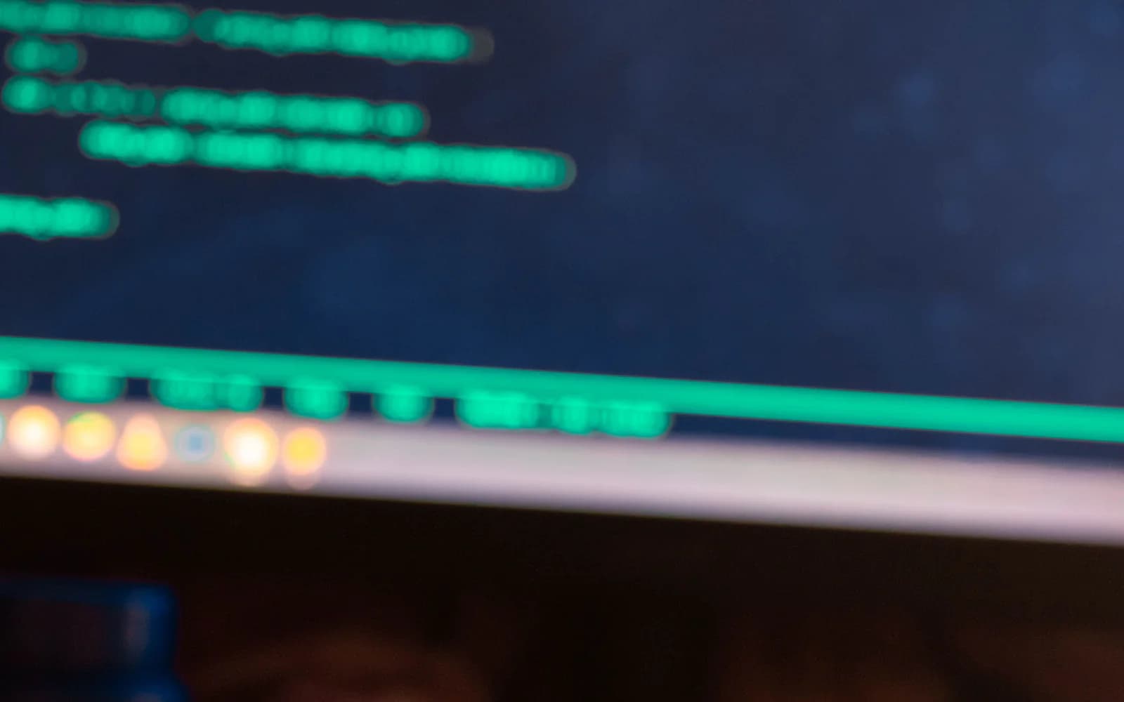 Green programming code on a dark monitor above a blurred keyboard edge.